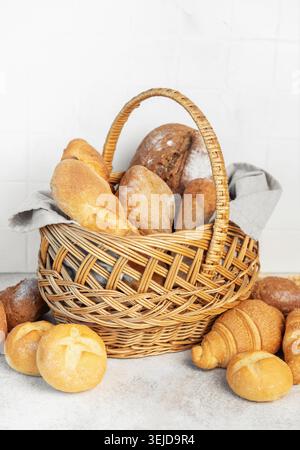 Korb gefüllt mit einer Vielzahl von frisch gebackenem Brot und Brötchen auf hellem Hintergrund Stockfoto