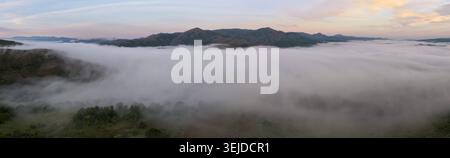 Panoramablick auf den Morgennebel, der das Tal in der Nähe von Bukmira mit Livadhez und Vela Bergen bei Sonnenaufgang bedeckt. Stockfoto