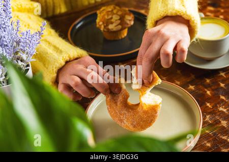 Frau in einem gemütlichen gelben Pullover, der einen Donut genießt Stockfoto