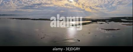 Ein Panoramablick auf dramatische Sonnenstrahlen, die bei Sonnenuntergang durch Wolken über den Feuchtgebieten brechen, und das ruhige Wasser der Patok Lagoon. Stockfoto