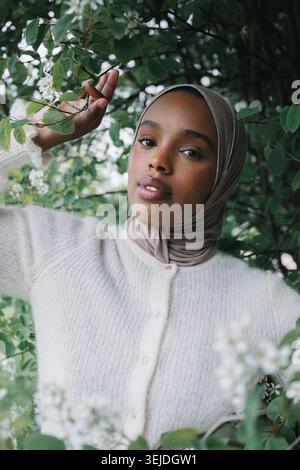 Junge muslimische Frau im Hijab zwischen blühenden Ästen im Frühlingspark Stockfoto