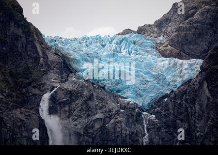 Ein atemberaubender blauer Gletscher hängt in einem felsigen Bergtal Stockfoto
