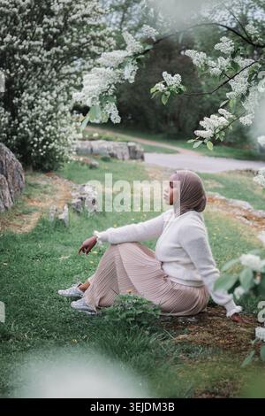 Junge muslimische Frau im Hijab, die sich unter blühenden Frühlingsbäumen entspannt Stockfoto