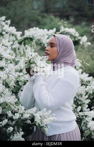 Anmutige muslimische Frau im Hijab, umgeben von blühenden Frühlingsblumen Stockfoto