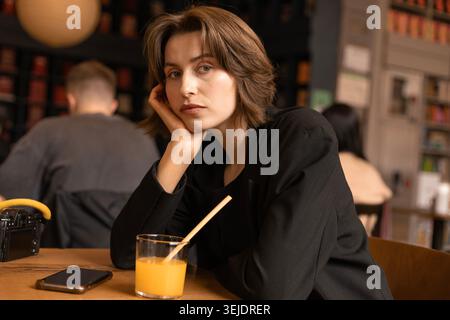 Eine junge Frau in Black Blazer am Cafe Table, die in die Kamera schaut Stockfoto