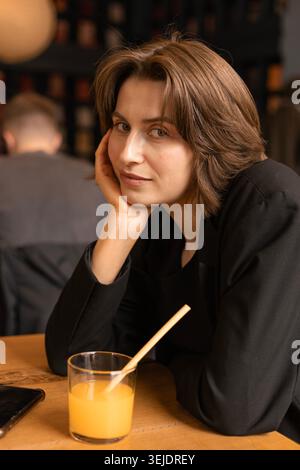 Junge Frau, die mit Orangensaft am Café-Tisch sitzt Stockfoto