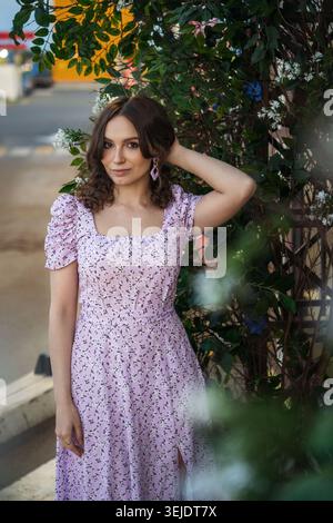 Junge Frau im lila Blumenkleid mit Blattspalier Stockfoto