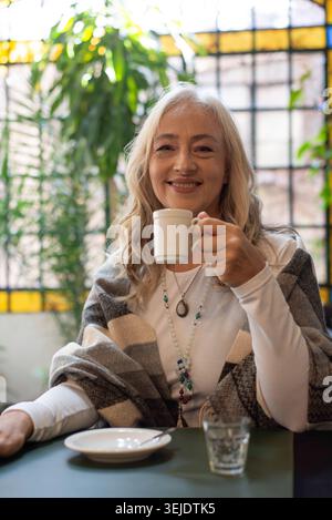 Lächelnde reife Frau, die in einem Café eine Tasse hält Stockfoto