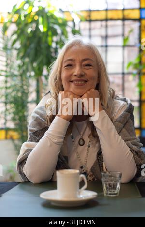 Lächelnde reife Frau, die in einem Café eine Tasse hält Stockfoto