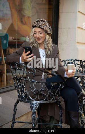 Überraschte reife Frau, die vor einem Café auf das Smartphone schaut Stockfoto