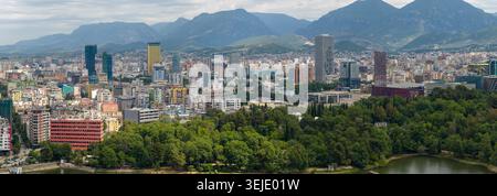 Wunderschönes, weites Panorama der dichten Tirana-Stadt mit modernen Hochhäusern, Grand Park-Bäumen und majestätischen Bergen. Stockfoto