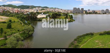 Wunderschönes, weites Panorama über den künstlichen See in Tirana mit üppigen grünen Ufern, modernen Gebäuden am See und Hügeln. Stockfoto