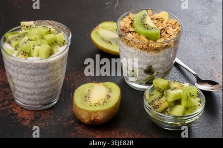 Zwei Gläser Chiasamenpudding, eines mit Kiwi-Würfel und das andere mit Müsli und Bananenchips, liegen auf einer dunklen Oberfläche Stockfoto