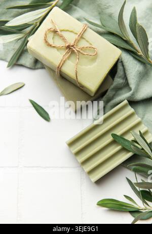 Natürliche Olivenseifenriegel mit Olivenzweigen auf weißen Fliesen Stockfoto