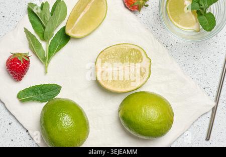 Ein Blick von oben auf die Zutaten für ein erfrischendes Getränk, einschließlich ganze und geschnittene Limetten, frische Minzzweige, leeres Glas, Metall Stockfoto