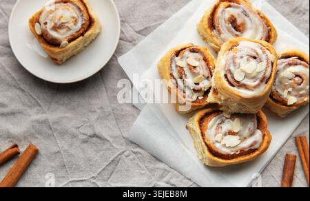 Köstliche Zimtrollen mit Glasur und Mandeln auf Backpapier Stockfoto