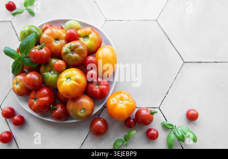Frische Tomaten auf einem weißen Teller mit grünen Basilikumblättern in einer hellen Küche Stockfoto
