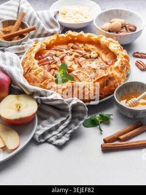 Köstlicher Apfelkuchen mit Mandeln, Honig und Zimt serviert auf einem Tisch mit frischen Äpfeln und Nüssen Stockfoto