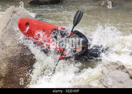 Intensiver fokussierter männlicher Kajak rollendes rotes Kajak im rauen Wildwasserfluss mit schwarzem Paddel inmitten von rasanten rasanten Outdoor-Abenteuern Stockfoto
