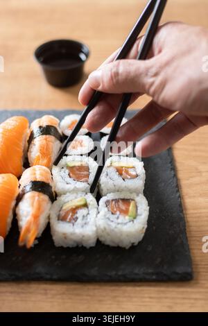 Frau isst Sushi mit Essstäbchen auf Holztisch. Nahaufnahme Stockfoto