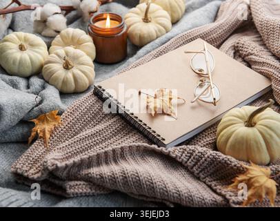 Herbstkomposition. Gemütliche Wohnatmosphäre mit Kerze, Notizblock, trockenen Blättern, dekorativen Kürbissen und Strickpullover Stockfoto