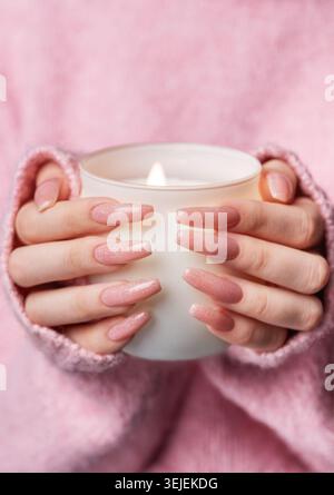 Eine Frau in einem rosa Pullover mit einer rosa Maniküre hält eine Kerze Stockfoto