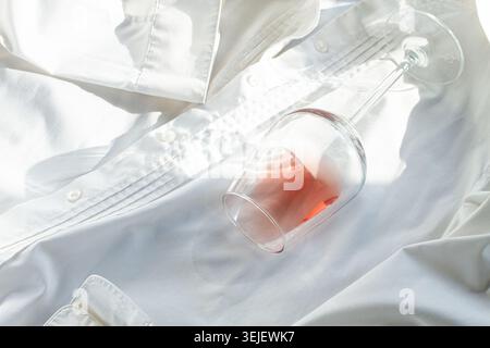 Glas, mit rosafarbenem Wein, verschüttet auf einem weißen Hemd, Nahaufnahme, selektiver Fokus, keine Leute, Konzept, Draufsicht, Stockfoto