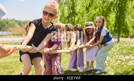 Kinder spielen im sonnigen Park während des Sommerspiels im Freien Tauziehen. Stockfoto