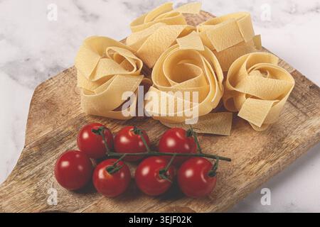 Rohe Pappardelle Nudeln, auf einem hölzernen Schneidebrett, mit Kirschtomaten, Blick von oben, keine Leute, Stockfoto
