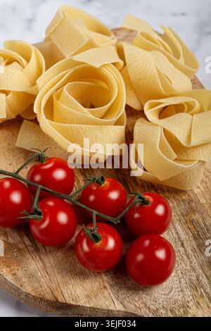 Rohe Pappardelle Nudeln, auf einem hölzernen Schneidebrett, mit Kirschtomaten, Blick von oben, keine Leute, Stockfoto