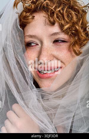 Charmante junge Frau mit lockigen Haaren lächelt in weichem, fließenden Stoff. Stockfoto