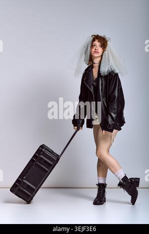 Die trendige junge Frau präsentiert Mode mit einem Koffer und trägt einen einzigartigen Look, der begeistert. Stockfoto