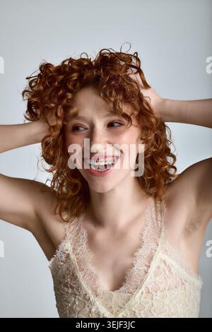 Die charmante junge Dame mit roten lockigen Haaren sorgt für einen lebendigen Moment und zeigt ihre lebendige Persönlichkeit. Stockfoto