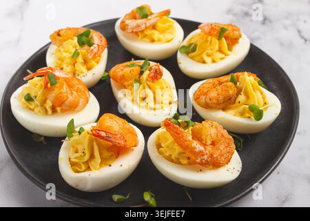 Gekochte Eier mit Eigelb gefüllt und mit Mayonnaise gewürzt, gefüllte Eier mit Garnelen, auf einem schwarzen Teller, selektiver Fokus, close-u Stockfoto