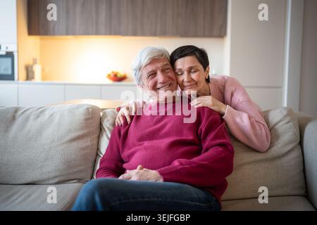 Liebevolles altes Paar umarmt sich zu Hause auf der Couch, hat Spaß und ruht sich zusammen aus. Bindung der Seniorenfamilie Stockfoto