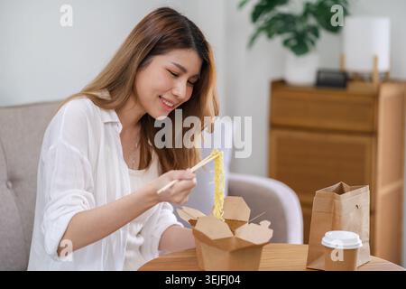 Asiatische Frau mit Essen und Getränken zum Mitnehmen zu Hause. Konsum Essen zu Hause Lieferessen. Genießen Sie köstliche Lieferung zum Mitnehmen leckere Mahlzeit. Stockfoto
