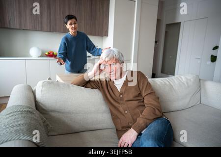 Müder Ehemann sitzt gleichgültig auf dem Sofa und ignoriert die wütende wütende, akribische Ehefrau, die die Schuld gibt Stockfoto