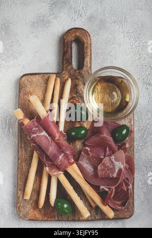 Eine Vorspeise aus Schinken, grissini und Oliven, serviert auf einem Holzbrett mit Olivenöl. Stockfoto