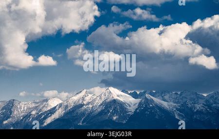 Aus der Ferne die schneebedeckten Gipfel der Tatra vor dem dramatischen blauen Himmel mit weißen Kumuluswolken. Alpenlandschaft mit majestätischer Schneedecke Stockfoto