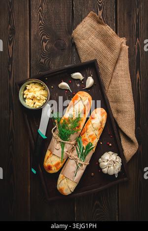 Baguette mit Knoblauchbutter und Kräutern, gebraten, auf einem braunen Holztisch, Blick von oben, rustikaler Stil, keine Leute, Stockfoto