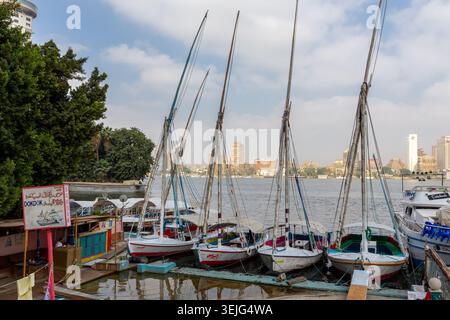 Kairo, Ägypten, 25.07.21. Ali Baba Hafen auf dem Nil in Kairo mit traditionellen Feluken-Ausflugsbooten und Gizeh Stadtbild im Hintergrund. Stockfoto