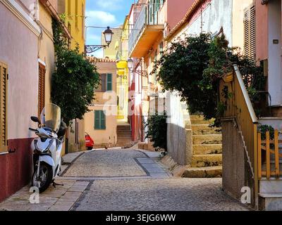 Eine malerische Straße mit lebhaften Pastellgebäuden und einem geparkten Roller in der mediterranen antiken Stadt La Maddalena, Italien Stockfoto