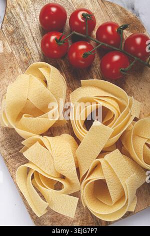 Rohe Pappardelle Nudeln, auf einem hölzernen Schneidebrett, mit Kirschtomaten, Blick von oben, keine Leute, Stockfoto