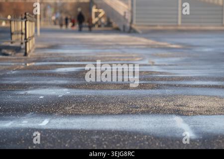 Enteisungsmittel auf Asphalt im Winter. Salzkörner auf eisiger Bürgersteig-Pflasterplatte mit technischem Salz Stockfoto