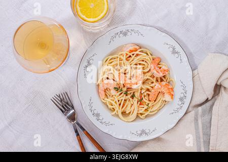 Pasta mit Garnelen und Thymian, serviert auf einem weißen Teller, mit einem Glas Weißwein, der Tisch ist gedeckt, es gibt keine Leute, Stockfoto
