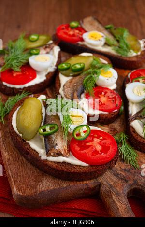 Offene Sandwiches mit Sprotten, Gemüse und Kräutern, auf Holzbrett, Frühstück, Snack, Stockfoto