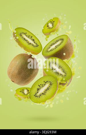 Frischer Kiwi-Saft mit frisch geschnittenen Kiwi-Fruchtscheiben in dynamischen Spritzern schweben im Fluss auf grünem Hintergrund. Ideal für die Entgiftung im Sommer Stockfoto