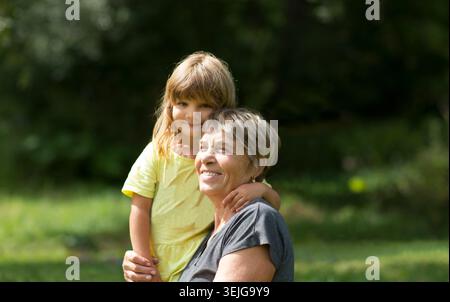 Kind Mädchen, das Großmutter umschließt und Zeit zusammen in der Natur verbringt. Konzept der freundlichen Familie. Qualitätszeit. Kopierbereich Stockfoto
