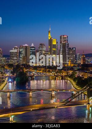 Luftaufnahme der beleuchteten Skyline von Frankfurt und der Flosserbrücke über dem Main während der blauen Stunde in Frankfurt am Main, Hessen, Deutschland. Stockfoto