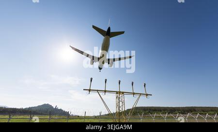 Flugzeug mit Fahrgestell, das über dem Kopf fliegt. Navigations- oder Landungsleuchte, die zur Piste im Hintergrund führt Stockfoto